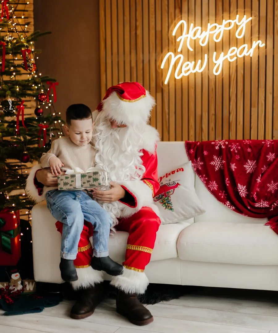 Санта-Клаус із хлопчиком і подарунком біля новорічної ялинки